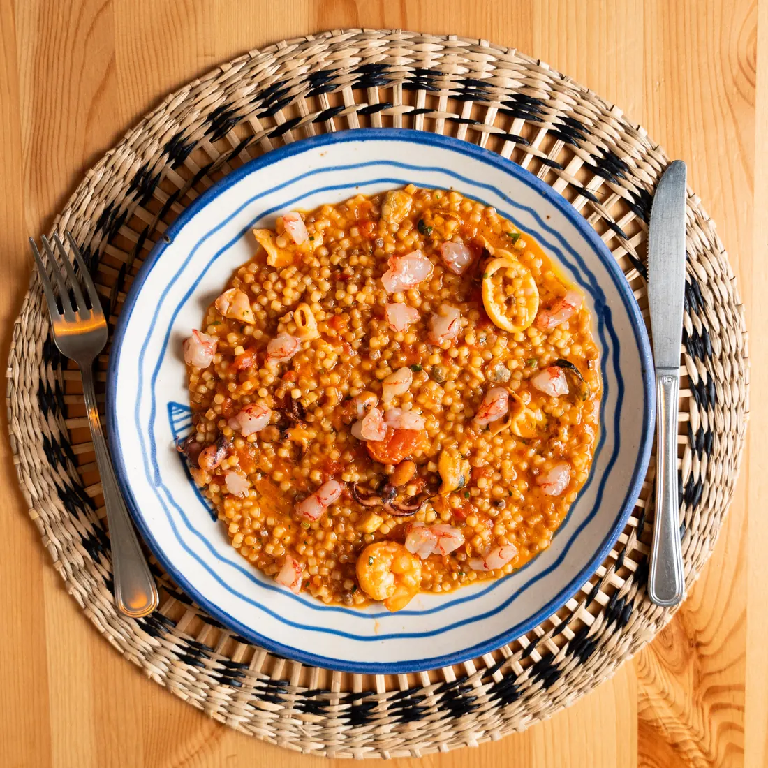 Fregola risottata allo scoglio servita in un piatto di ceramica